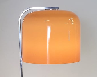 Puede incluir: Una lámpara de pie de cromo con un brazo curvo y una pantalla grande, redonda y de vidrio naranja.