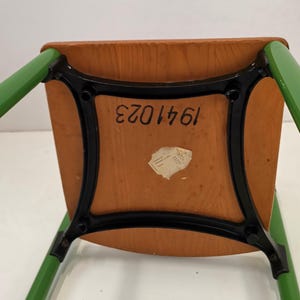 May include: The underside of a green wooden chair with black metal legs. The chair has a label with the number 1641023.