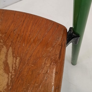 May include: A wooden chair with a green metal frame and black metal accents. The chair has a worn wooden seat.