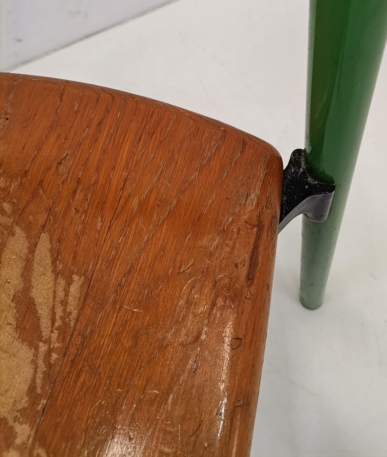 May include: A wooden chair with a green metal frame and black metal accents. The chair has a worn wooden seat.