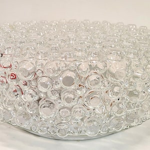 May include: A clear glass ceiling light fitting with a bubble design. The fitting is round and has a series of small, round, bubble-like protrusions covering the surface. The light fitting is designed to be mounted on a ceiling.