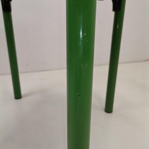 May include: Close-up of a green metal chair leg with a few small scratches. The chair is made of metal and has a wooden seat.