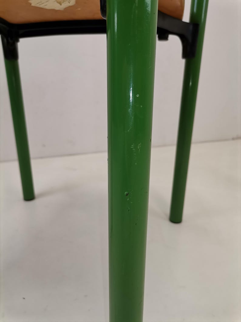 May include: Close-up of a green metal chair leg with a few small scratches. The chair is made of metal and has a wooden seat.