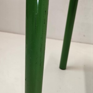 May include: Close-up of a green metal chair leg with visible scratches and wear. The leg is round and has a smooth finish.