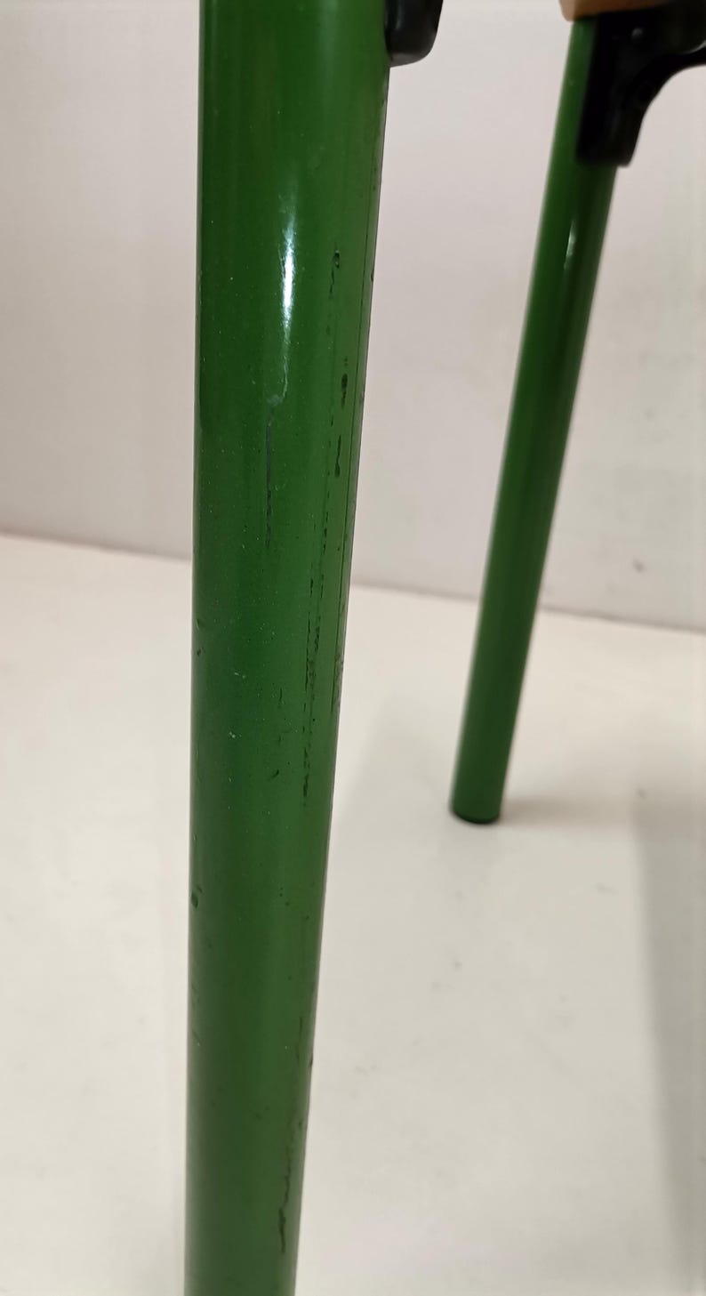 May include: Close-up of a green metal chair leg with visible scratches and wear. The leg is round and has a smooth finish.