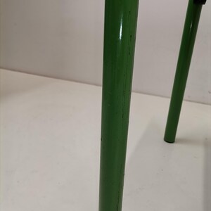 May include: Close-up of a green metal chair leg with visible scratches and wear. The leg is round and has a smooth, glossy finish.