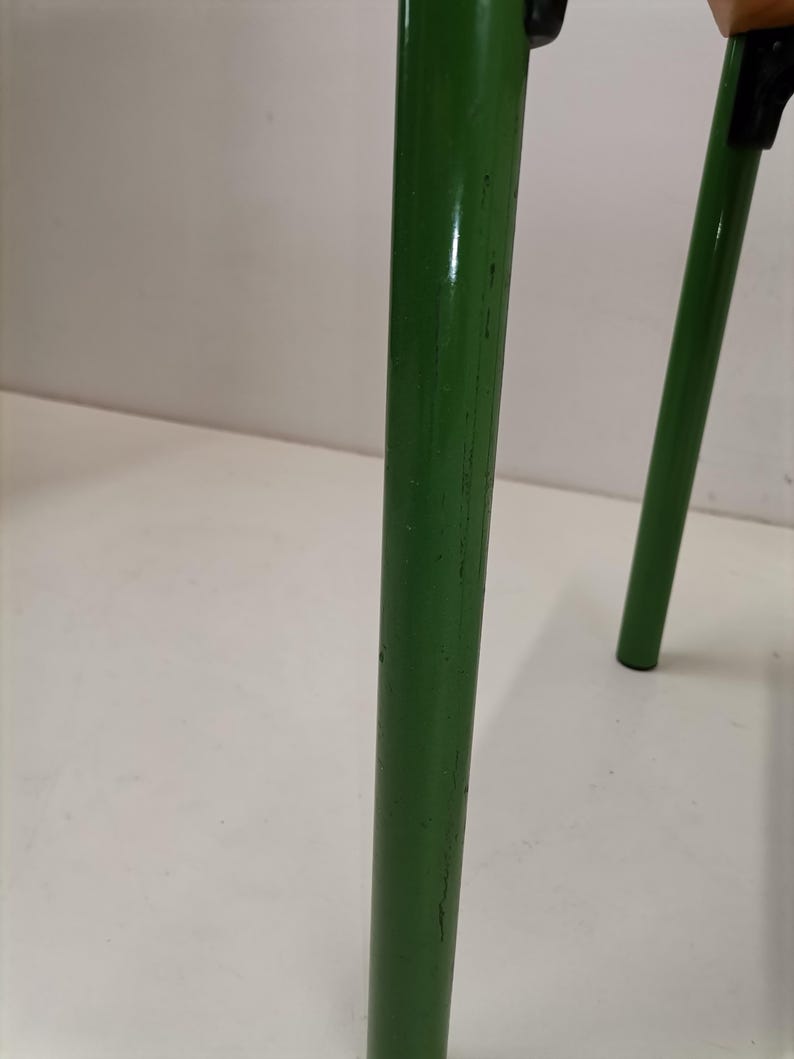 May include: Close-up of a green metal chair leg with visible scratches and wear. The leg is round and has a smooth, glossy finish.