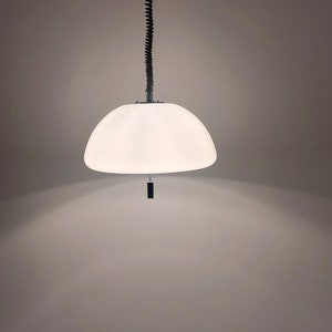 May include: A white, dome-shaped pendant light fixture. The light hangs from a black, coiled cord attached to a metal rod and a ceiling mount. The fixture has a black pull cord. The light is turned on, illuminating the room.