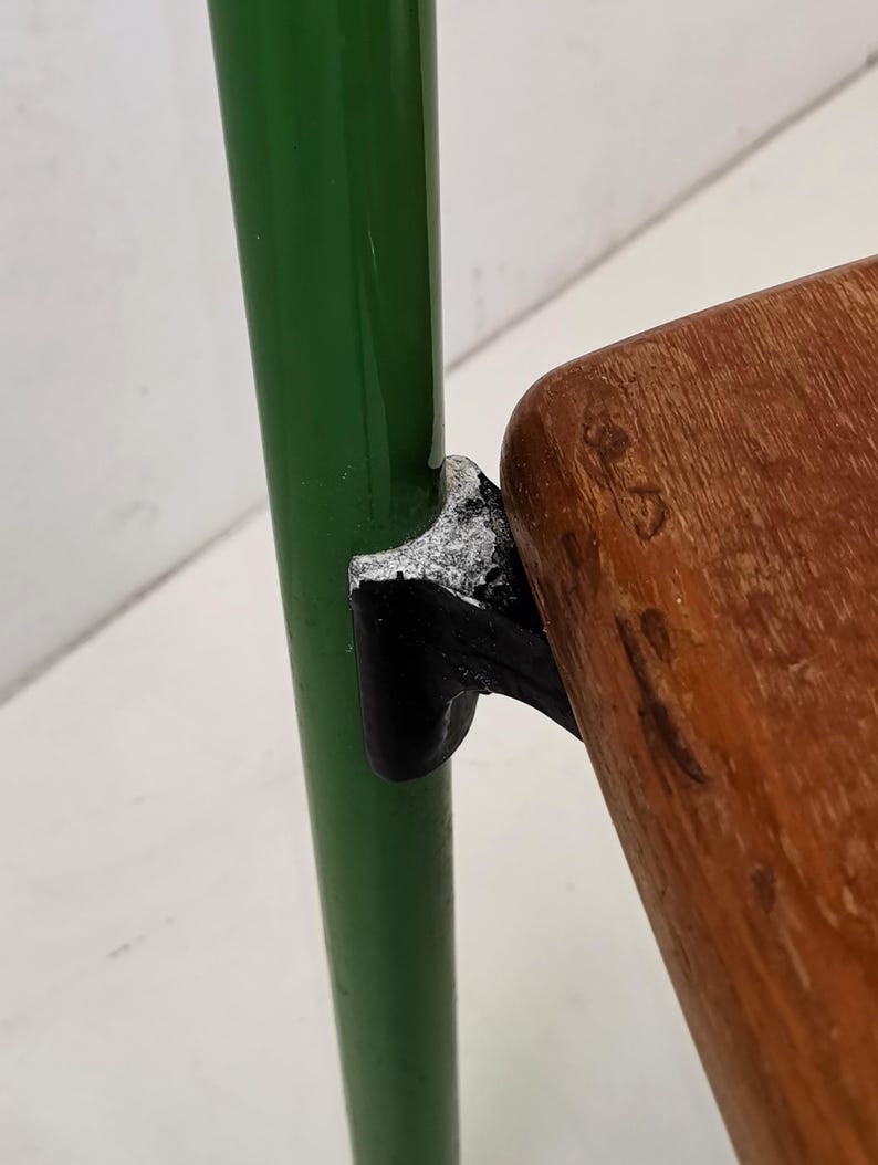 May include: Close-up of a green metal chair leg with a black metal bracket connecting to a wooden seat. The wood has a natural grain pattern.