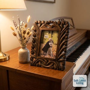 May include: A rectangular dark brown wooden picture frame with an intricate carved scrollwork border. The frame holds a photograph of a person hugging a dog in a forest setting, with the text "Weloo Home" visible in the upper corner of the photo.