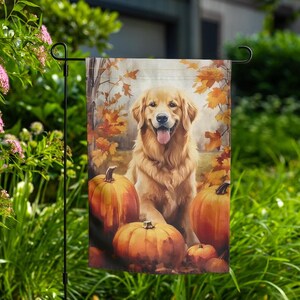 May include: A garden flag depicting a Golden Retriever dog surrounded by pumpkins and autumn leaves. The dog is smiling with its tongue out. The pumpkins are orange, and the leaves are various shades of orange and brown.