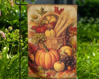 May include: A garden flag featuring a fall harvest scene. The flag displays a basket overflowing with pumpkins, grapes, and wheat. The color palette includes shades of orange, red, and yellow, with a beige background. The flag is hanging on a black metal stand.