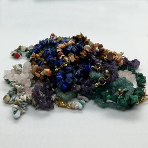 May include: A pile of colourful gemstone beads, including blue, green, purple, pink, and brown. The beads are made of various materials, such as lapis lazuli, amethyst, rose quartz, and jasper.