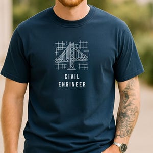 May include: A dark blue short-sleeved t-shirt featuring a white line-art graphic of a bridge structure over a grid pattern. Below the graphic, the text "CIVIL ENGINEER" is printed in a clean, white, sans-serif font centered on the chest.