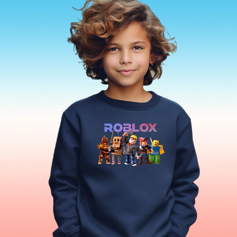 Pu&ograve; includere: Felpa blu navy con la scritta "ROBLOX" in un gradiente viola e blu. Sotto il testo ci sono personaggi dei cartoni animati. La felpa &egrave; indossata da una persona con i capelli castani ricci.