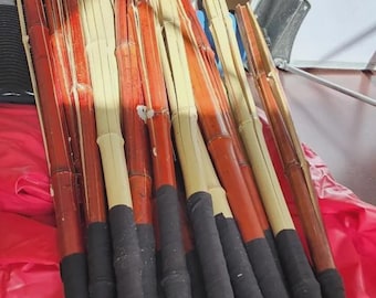 May include: A collection of long, slender bamboo sticks featuring alternating natural light beige and reddish-brown stained segments. Each stick has a black wrapped handle at the base, providing a textured grip for these cylindrical wooden poles.