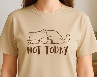 May include: A sand-colored t-shirt featuring a cartoon cat illustration and the words "NOT TODAY" in a dark brown font. The cat is lying down with its eyes closed. The shirt is a crew neck style.