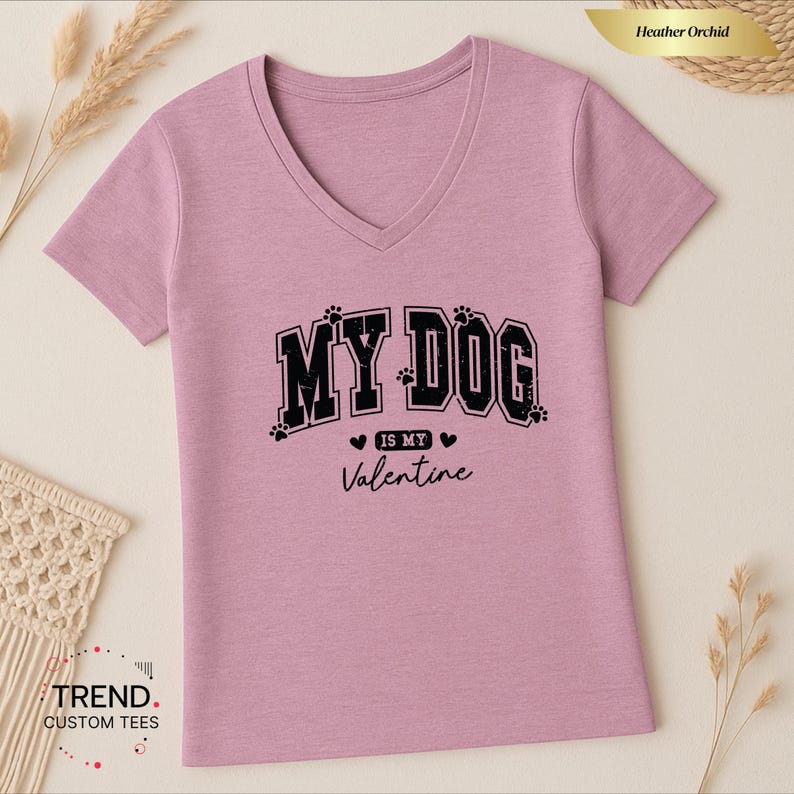 May include: Heather orchid V-neck t-shirt with the text "MY DOG is my Valentine" in black. The text includes paw prints and hearts. The shirt is a light purple color.
