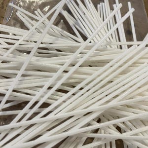 May include: A pile of white, thin, flexible sticks. The sticks are bundled together and appear to be made of a lightweight material.