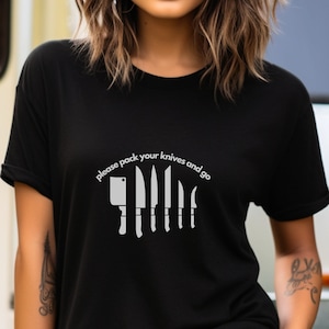 May include: A black t-shirt with a white graphic of knives and the text "please pack your knives and go".