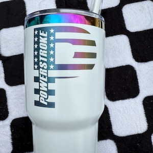 May include: White stainless steel tumbler with a black and white American flag design and the text "POWERSTROKE" printed on the side. The tumbler has a rainbow iridescent finish and a clear plastic straw.