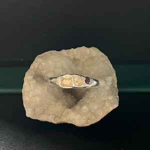 May include: A silver ring with three small stones, two yellow and one red.