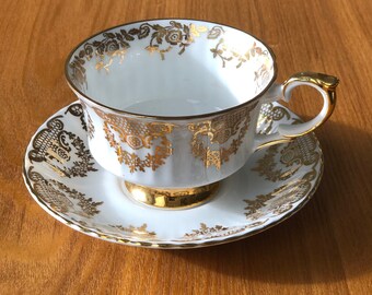 Puede incluir: Una taza de té y un platillo blancos con ribetes dorados y un delicado patrón floral. La taza y el platillo están hechos de porcelana fina y tienen un diseño clásico.