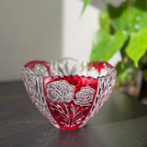 May include: A clear, cut-glass bowl with a vibrant red interior. The bowl features a floral design, with roses and leaves carved into the glass. The bowl is likely used for decorative purposes.