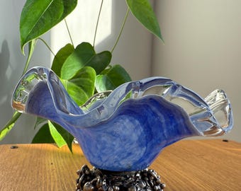 May include: A decorative glass bowl with a wavy rim, featuring a blue and white marbled design. The bowl sits on a silver-colored metal base with a fruit-like pattern. The bowl is a decorative item.
