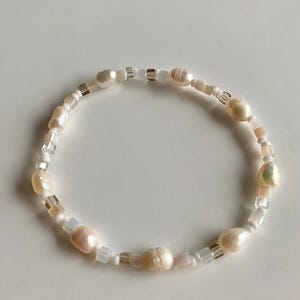 Peut inclure: Un bracelet délicat composé de perles blanches et crème et de petites perles claires et dorées.