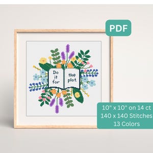 May include: Cross-stitch art in a wooden frame. The design features an open book with the text "Do it for the plot" surrounded by colorful flowers and foliage. The dimensions are 10" x 10".
