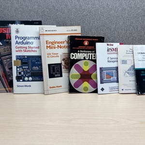 May include: A collection of technical books on a light-colored surface. Titles include "Programming Arduino," "Engineer's Mini-Note," and "A Dictionary of Computer." The books cover topics like electronics, computer science, and IT service management.