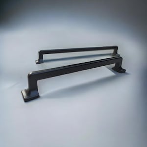 May include: Two matte black metal cabinet pulls with a rectangular bar design and curved feet. Each handle features a smooth, solid finish with a clean, linear silhouette, positioned one behind the other to show the hardware structure clearly.
