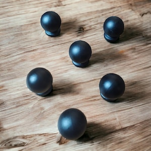 Puede incluir: Cinco pomos esféricos para armarios con un acabado negro mate liso. Cada pomo presenta una parte superior redondeada y una pequeña base circular, dispuestos en un patrón disperso. Los pomos tienen un color negro sólido y forma uniforme.