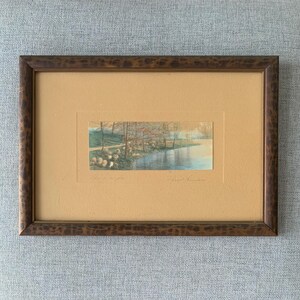 May include: A framed print of a watercolor painting depicting a forest scene with a river and trees. The print is matted and has a brown wooden frame.