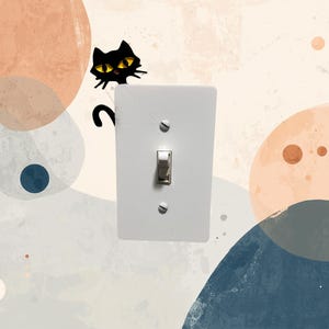 May include: A white light switch cover with a silver toggle switch and two screws. A black cat illustration with yellow eyes and a curved tail is positioned above the switch, adding a playful touch to the design.