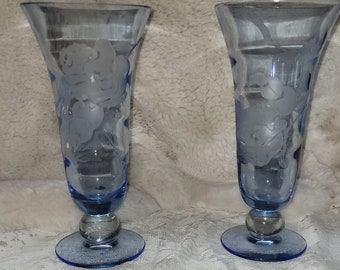 May include: Two blue glass goblets with etched floral designs. The goblets have a flared top and a round base.