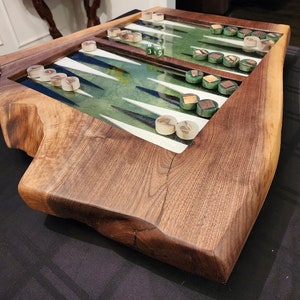 May include: A wooden backgammon board with a green and white playing surface. The board is made from a live edge slab of wood and has a natural, rustic look.