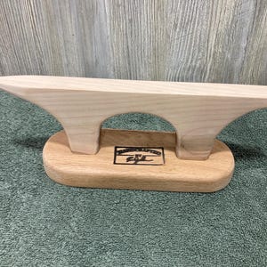 Può includere: Supporto per barche in legno con due archi e una base. La base ha il testo "Handcrafted by E.S.L." inciso.