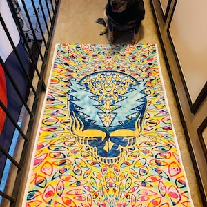 Puede incluir: Un tapiz psicodélico colorido con un cráneo con ojos y un diseño de rayo. El tapiz es amarillo, azul, rojo y verde.