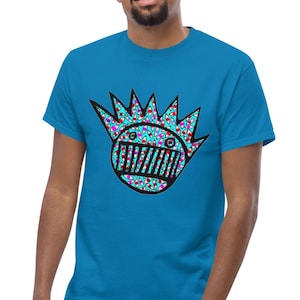 Puede incluir: Una camiseta azul turquesa con un estampado gráfico de una cara de dibujos animados con ojos y boca. La cara está rodeada por una corona de púas.