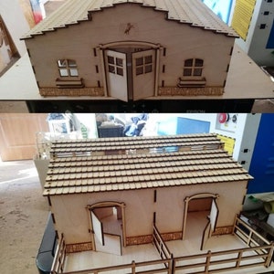 Puede incluir: Un modelo de madera de un granero con techo de tejas, dos establos y un área cercada. El granero tiene dos puertas y dos ventanas. El modelo está hecho de madera marrón claro.