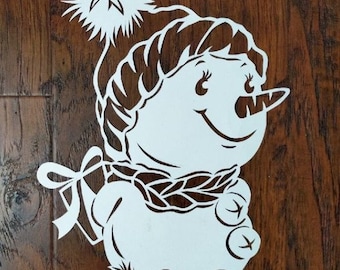 May include: White paper cut-out of a snowman wearing a hat and scarf with a pom-pom on top. The snowman has a carrot nose and two black buttons.