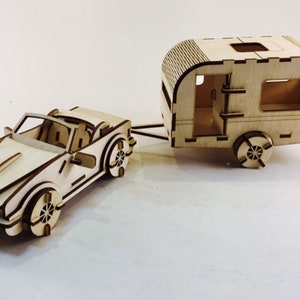 May include: A wooden model of a convertible car pulling a wooden model of a camper trailer. Both are made of light brown wood and have detailed features.