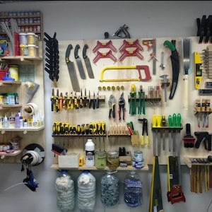 Op de afbeelding: Een aan de muur gemonteerde gereedschapsorganisator met een verscheidenheid aan gereedschappen, waaronder zagen, klemmen, linialen en schroevendraaiers. De gereedschappen zijn georganiseerd per type en kleur, en de organisator is gemaakt van hout.