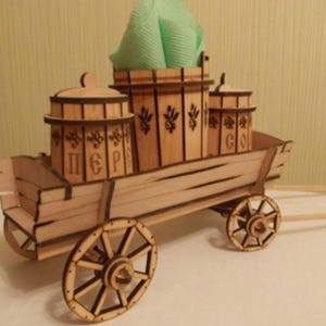 Może przedstawiać: Drewniany wóz z czterema kołami i uchwytem. Wóz jest ozdobiony zielonym materiałem i czterema drewnianymi pojemnikami z pokrywkami. Pojemniki są oznaczone słowami "ПЕР" i "С".