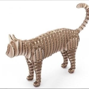 Könnte beinhalten: Eine stehende Katzenskulptur aus Wellpappe. Die Katze hat ein gestreiftes Muster und einen gebogenen Schwanz. Die Skulptur ist hellbraun und hat ein dreidimensionales Design.