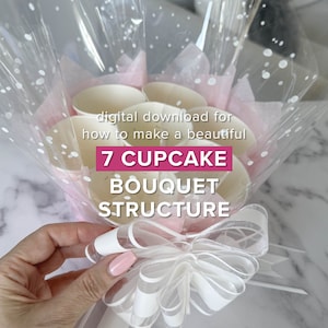 May include: A digital download for a 7 cupcake bouquet structure. The bouquet is wrapped in clear cellophane with white polka dots and a white ribbon with a bow. The bouquet is made with white cupcake liners.