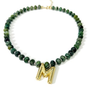 May include: A green gemstone beaded necklace with a gold letter M pendant.