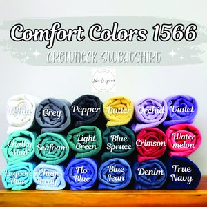 May include: A display of rolled-up Comfort Colors 1566 crewneck sweatshirts in various colors, including white, grey, pepper, butter, orchid, violet, chalky mint, seafoam, light green, blue spruce, crimson, watermelon, lagoon blue, chambray, flo blue, blue jean, denim, and true navy.